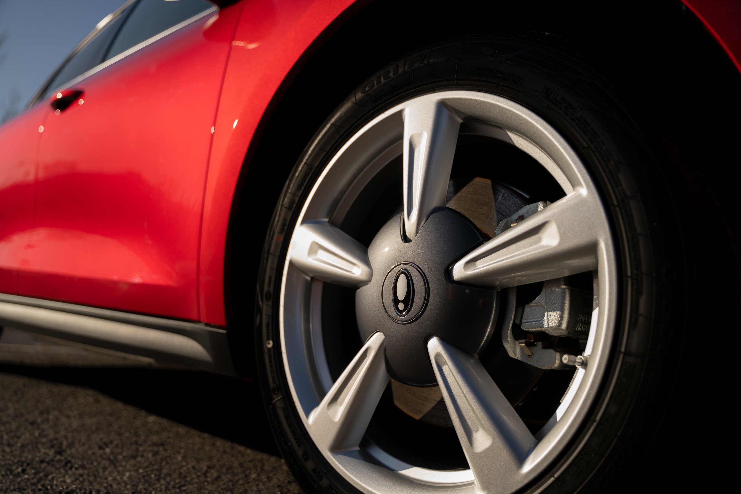 Close-up of a red car's wheel with a silver rim, parked on a road.