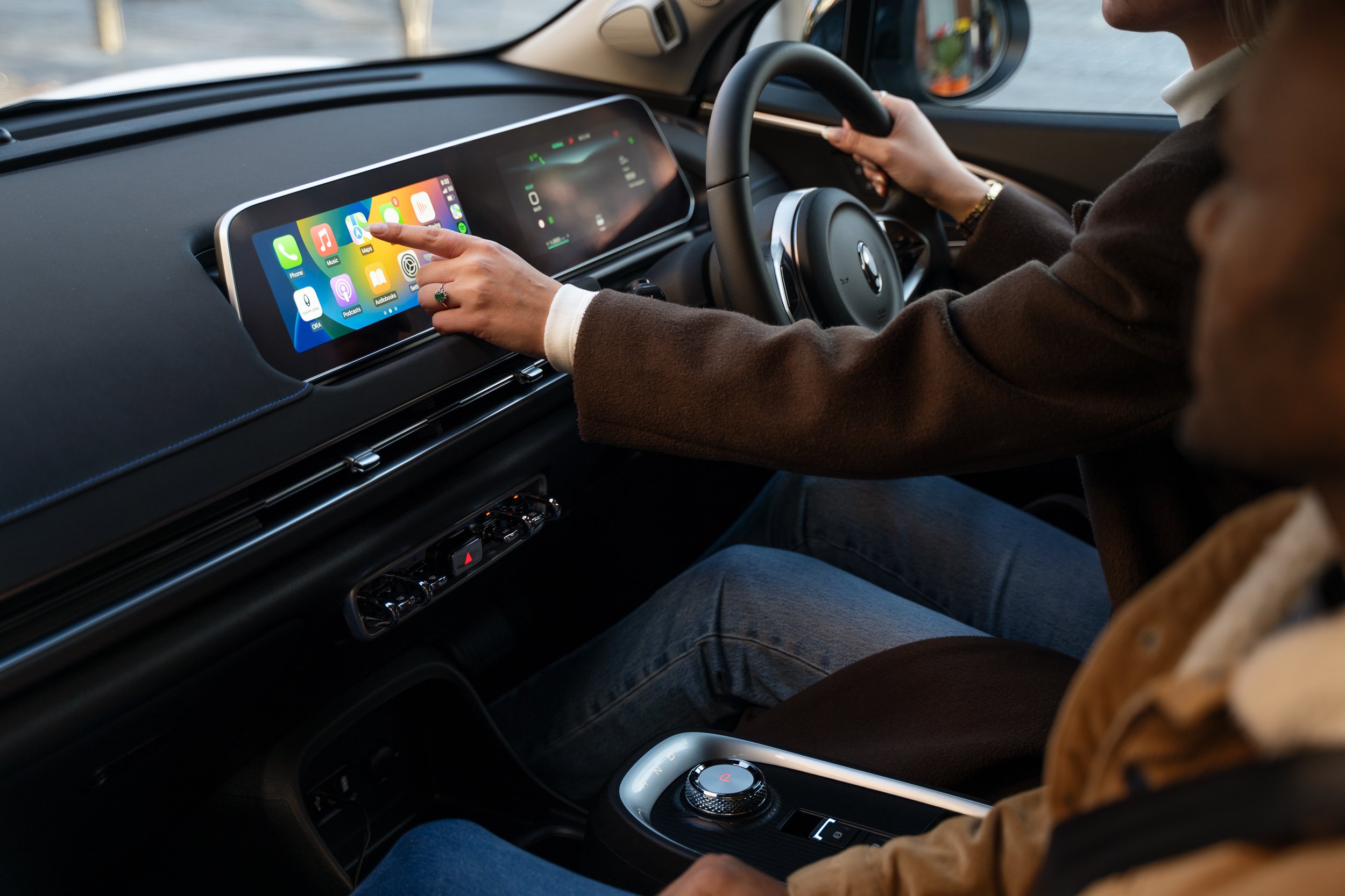 A person is using a smartphone with Apple CarPlay on the car's dashboard while sitting in the driver's seat of a BMW vehicle.