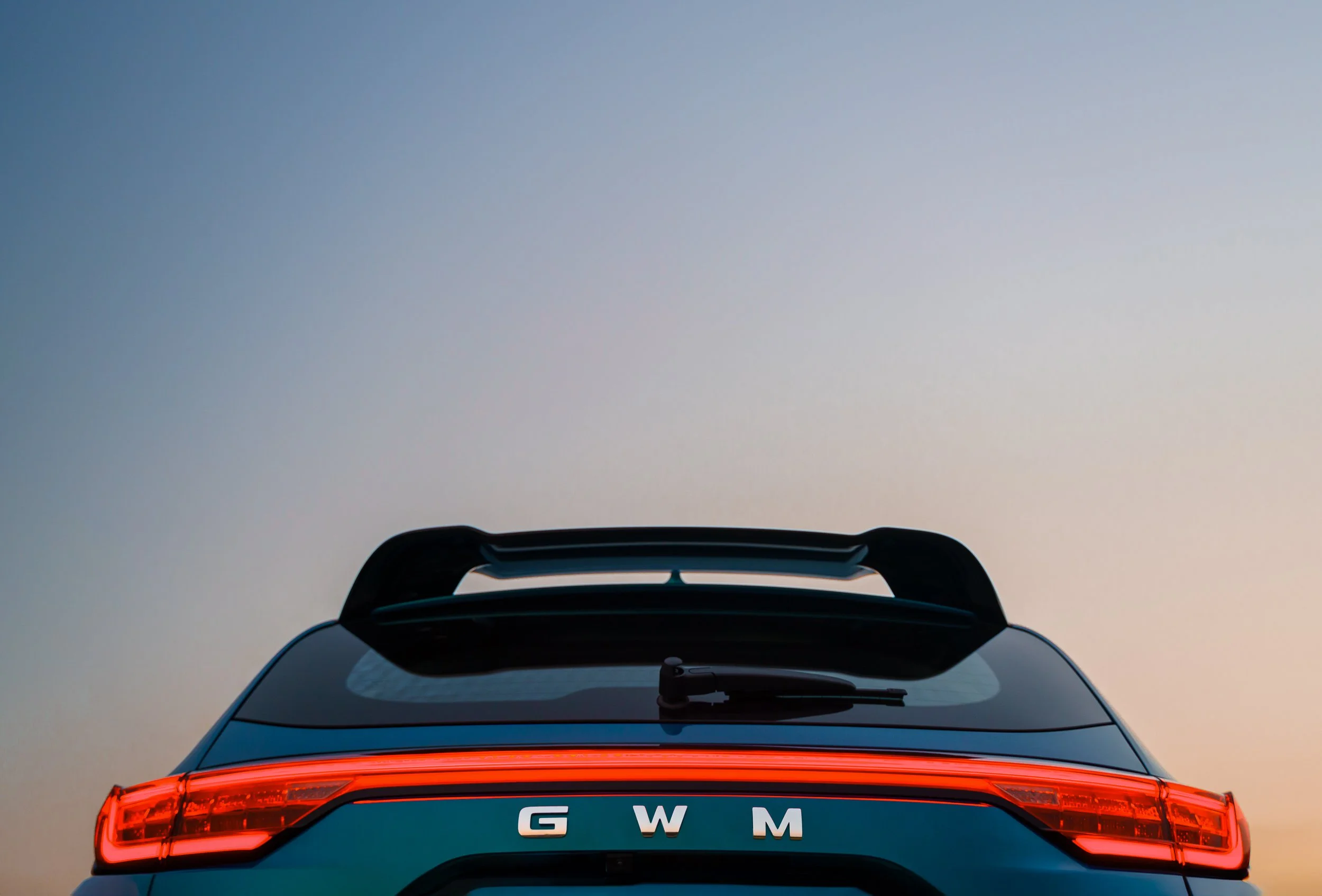 Rear view of a blue BMW car with illuminated taillights and a sunroof, photographed from a low angle against a clear sky.