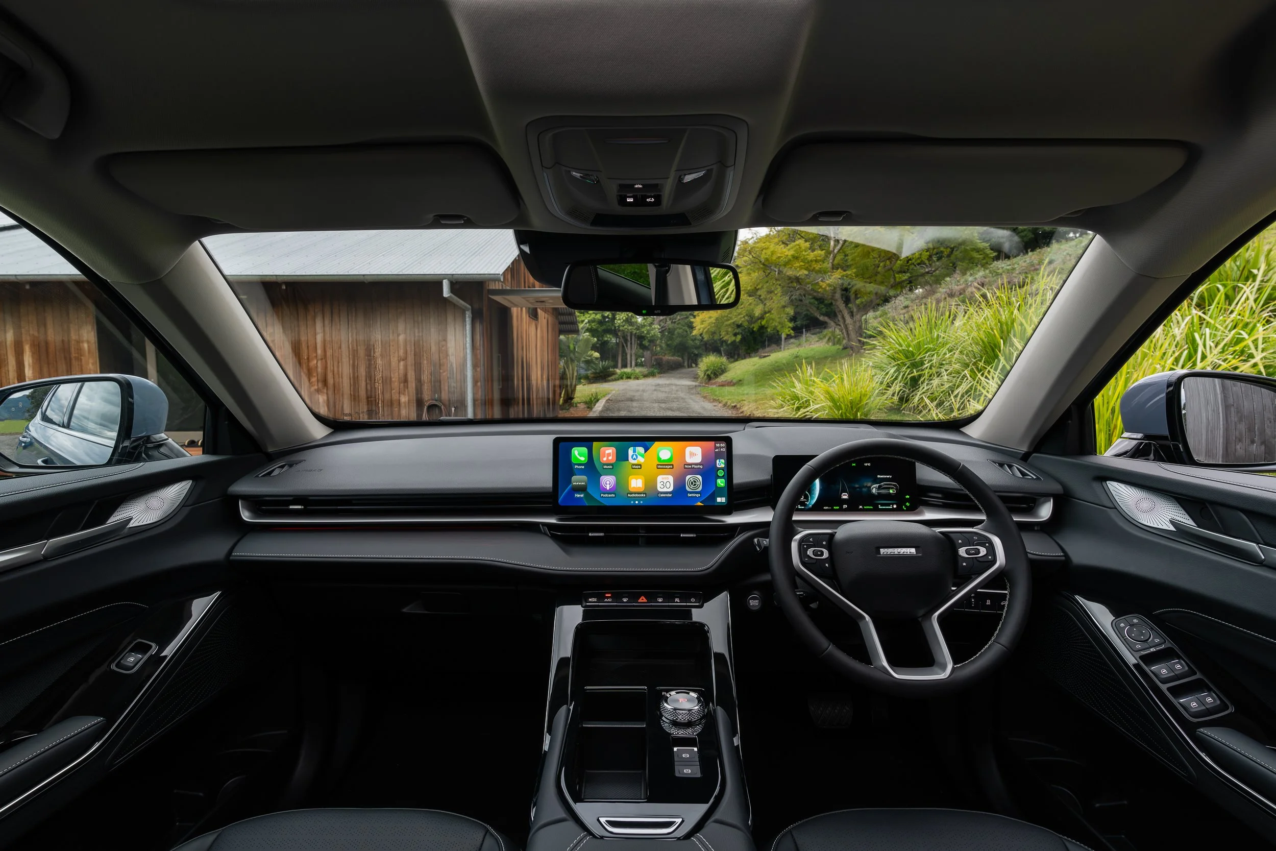The interior view of a modern car's dashboard and front seats, with a digital display screen showing apps, and a scenic outdoor background seen through the windshield.