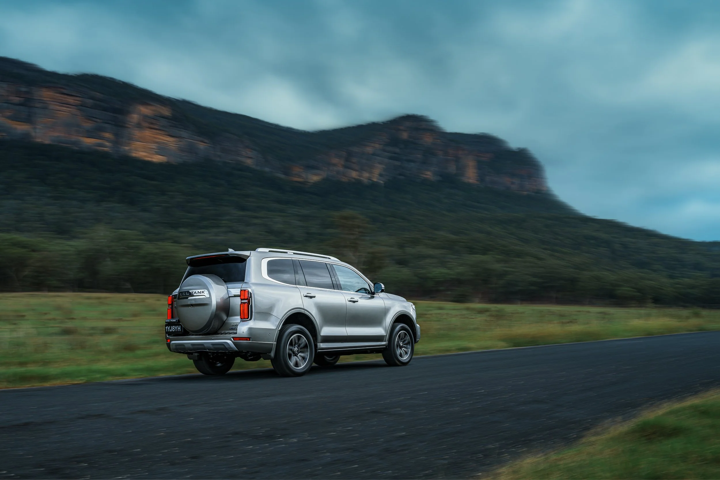 A silver SUV driving on a highway with mountains and cloudy sky in the background.