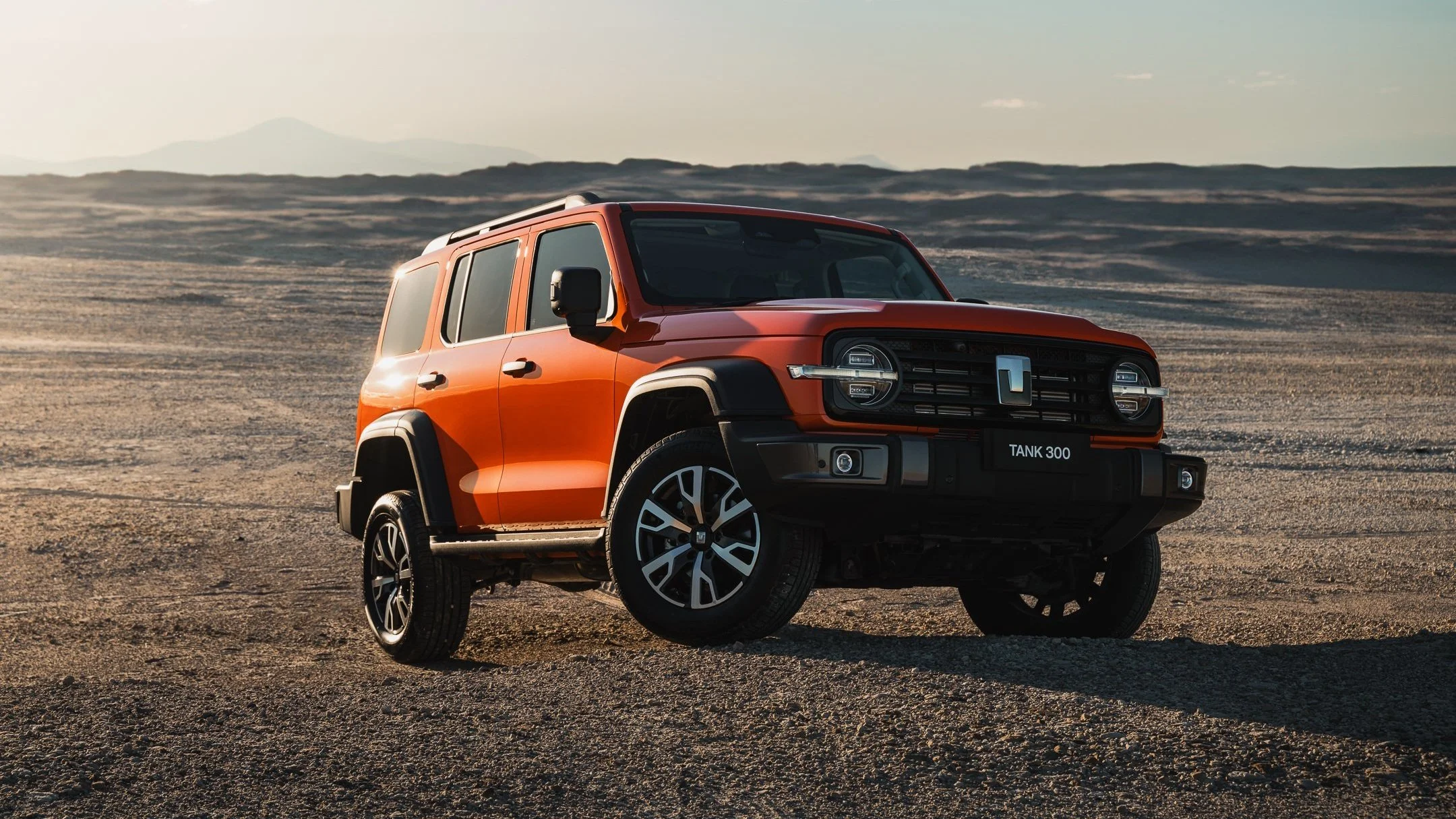 An orange SUV off-road vehicle in a desert landscape with mountains in the background.