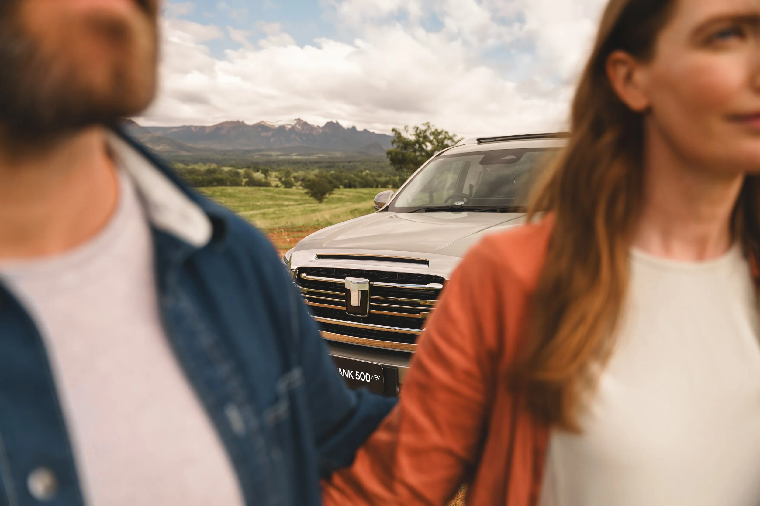 Close-up of two women in the foreground, with a silver pickup truck and scenic mountainous landscape in the background.