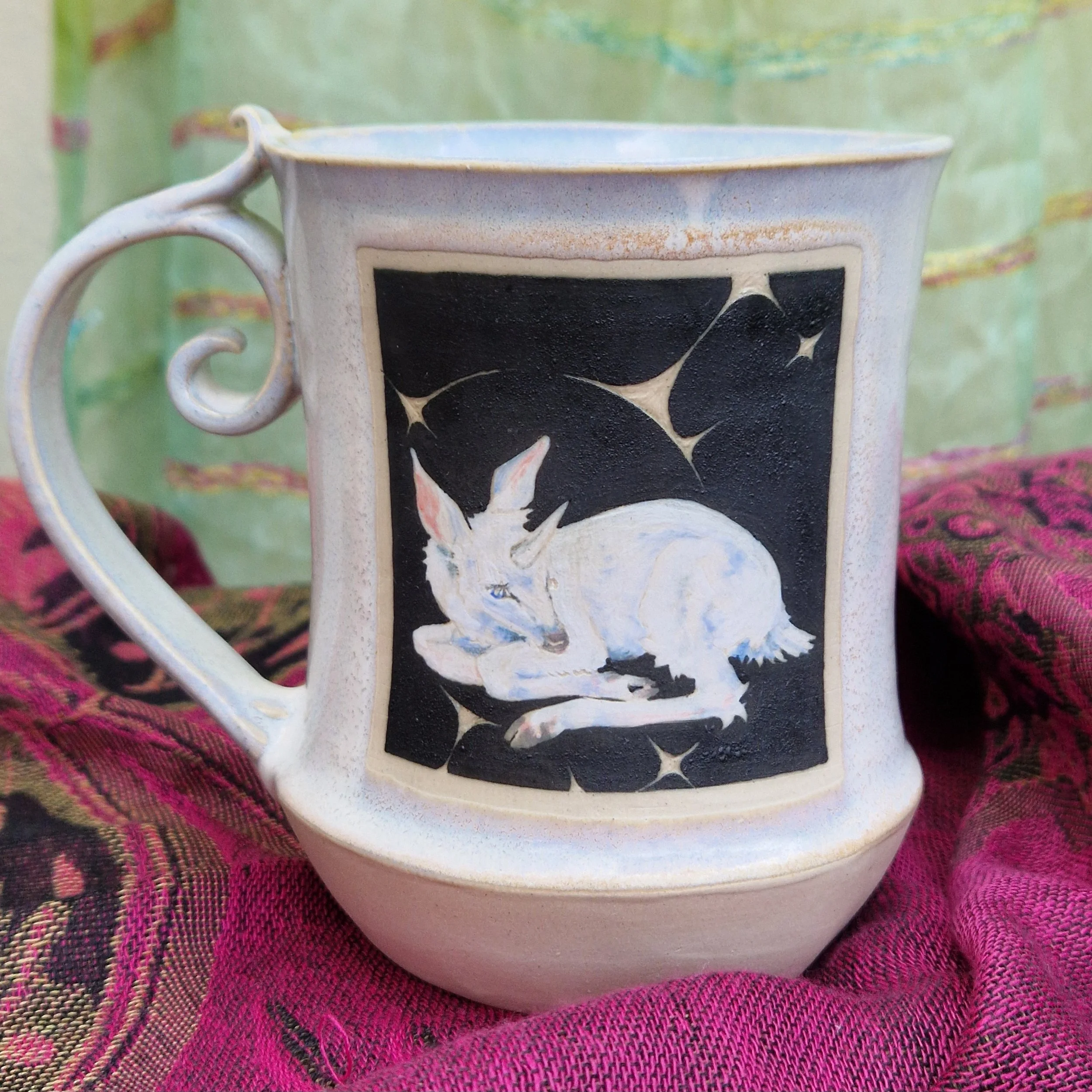 Close-up of a ceramic mug with a black and white abstract design, placed on a pink woven fabric.