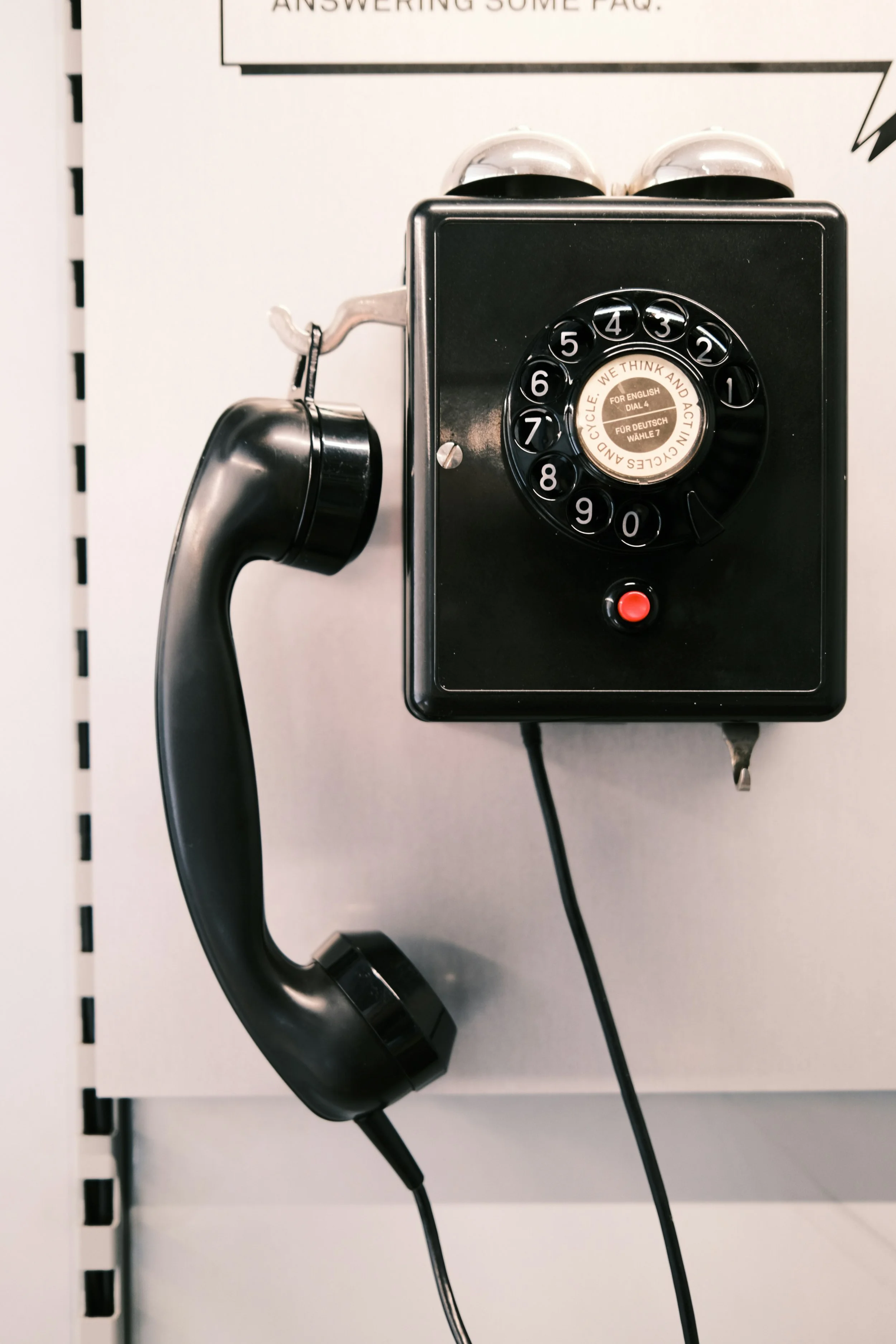 An old-fashioned black rotary phone attached to a wall, with the receiver hanging on the side, and a black cable connected to it.