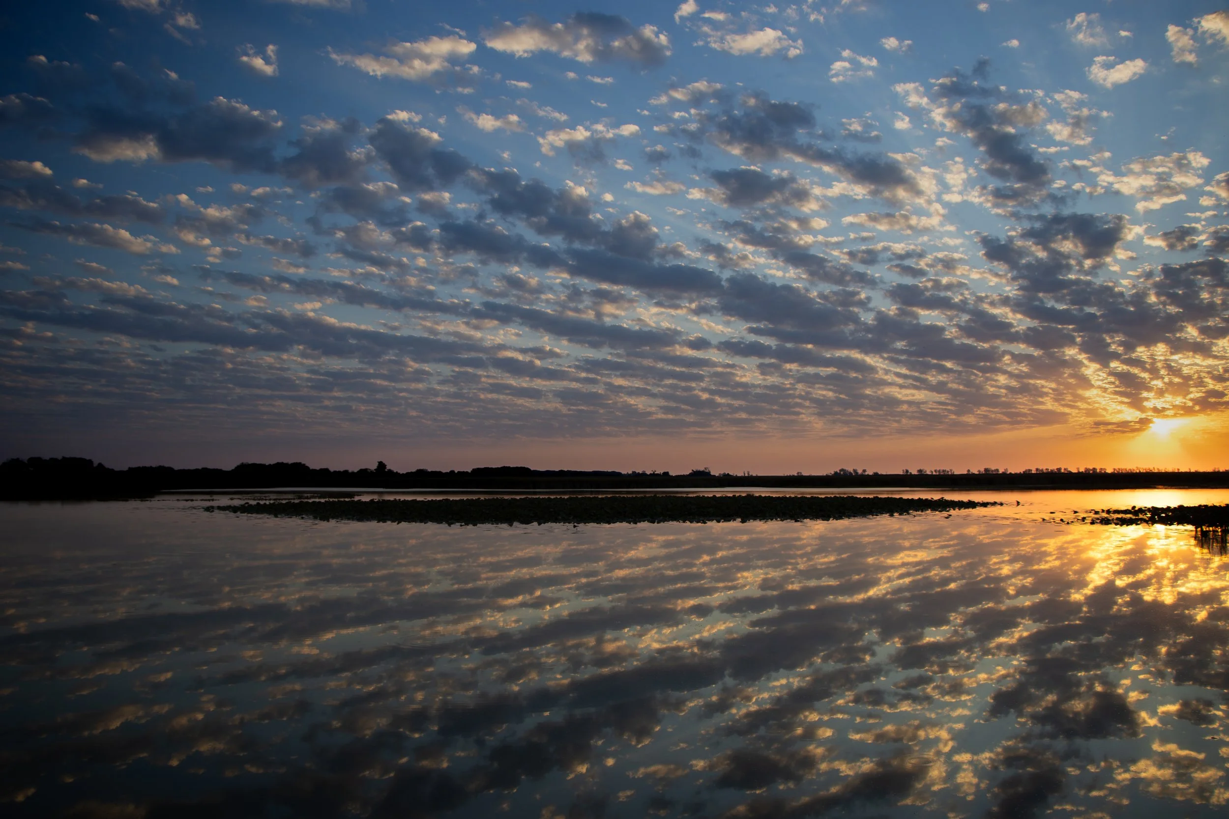 Sunset over a body of water with a partly cloudy sky.