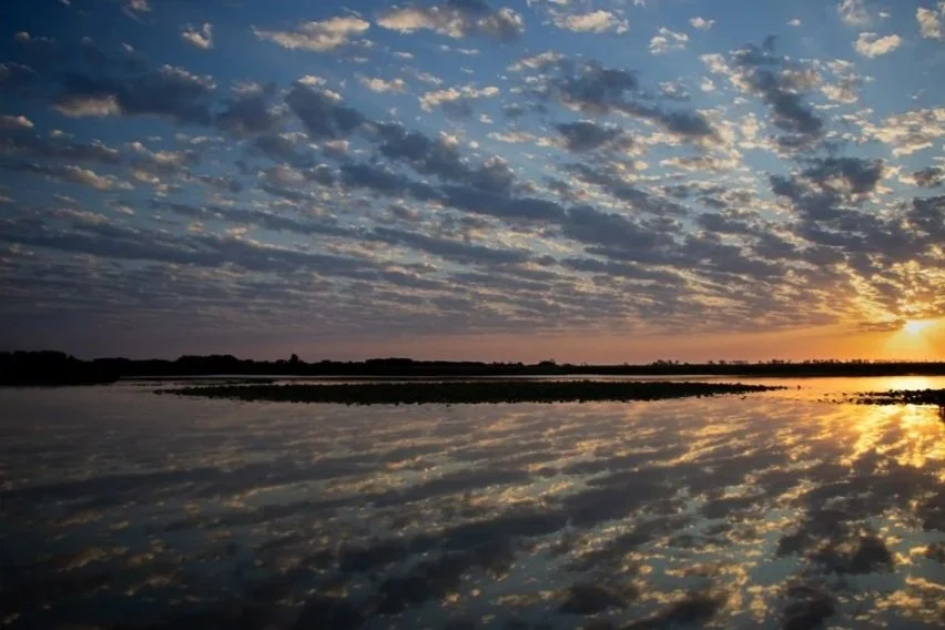Sunset over a body of water with reflections of clouds and the sky, creating a serene and picturesque landscape.