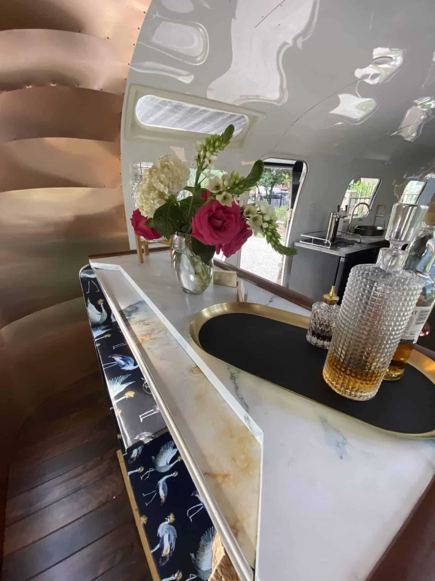A floral arrangement with pink and white flowers on a marble countertop in a modern kitchen setting, with mirrors and a reflective ceiling.