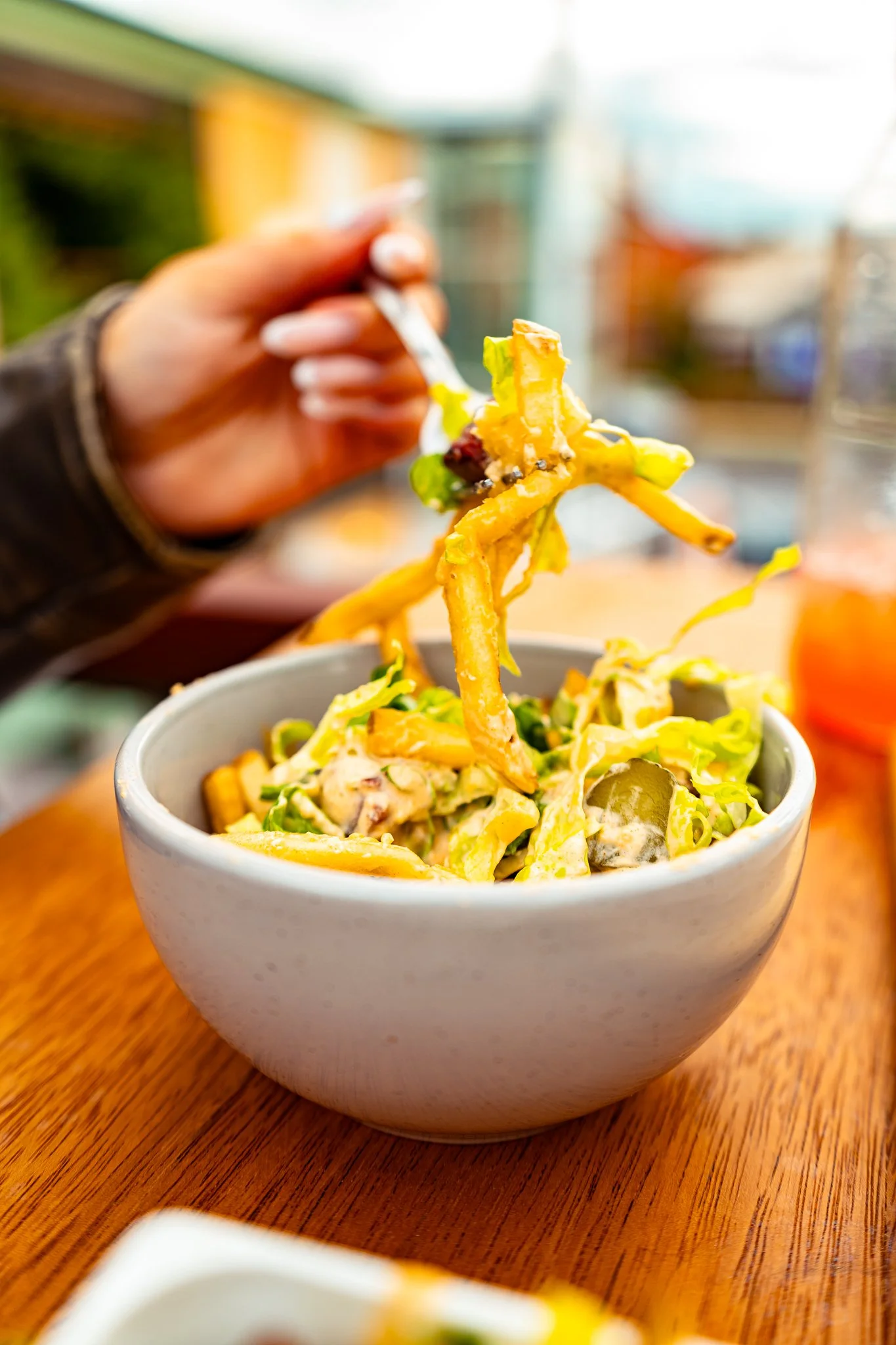 A bowl of salad with shredded lettuce, cheese, and other vegetables on a wooden table, with a person holding chopsticks picking up a piece of food.