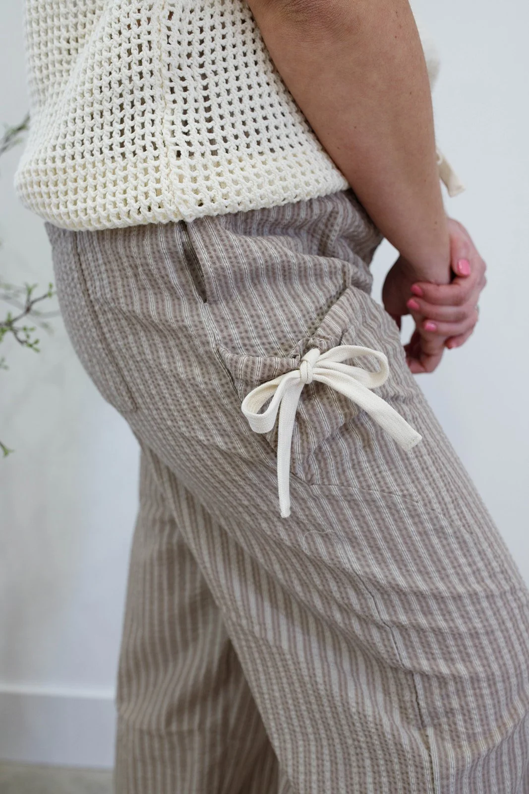 A person wearing beige striped pants with a drawstring and a cream-colored knitted top, holding their stomach.