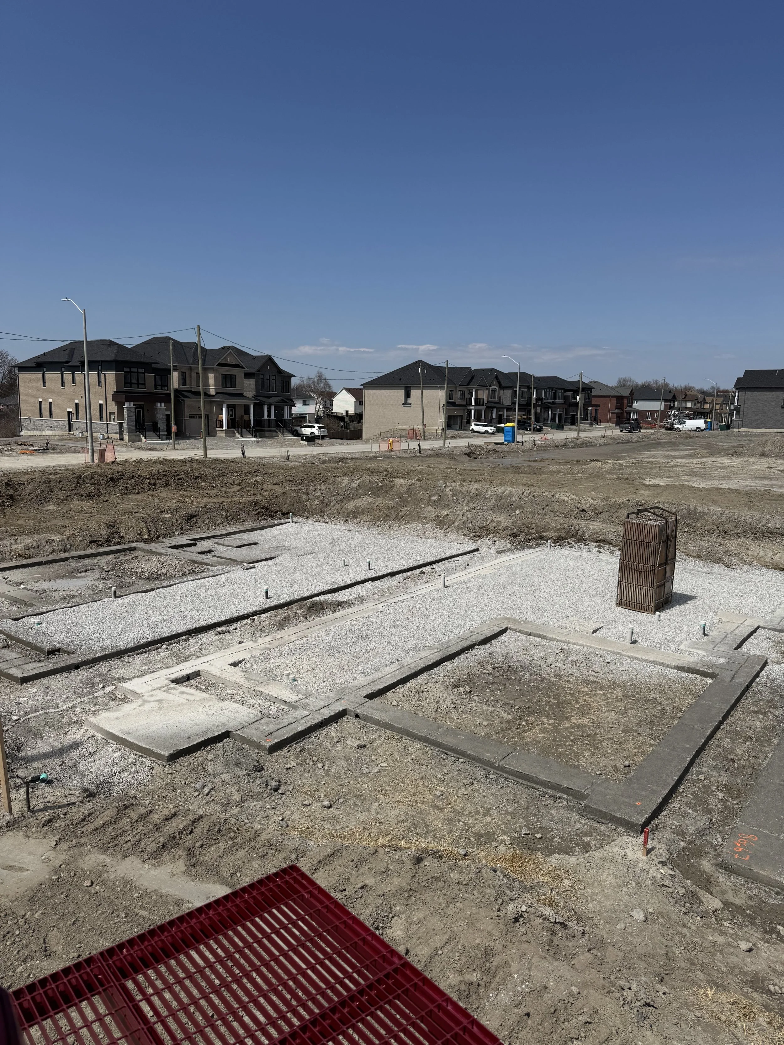 Construction site with foundation work and partially built homes in the background under a blue sky.