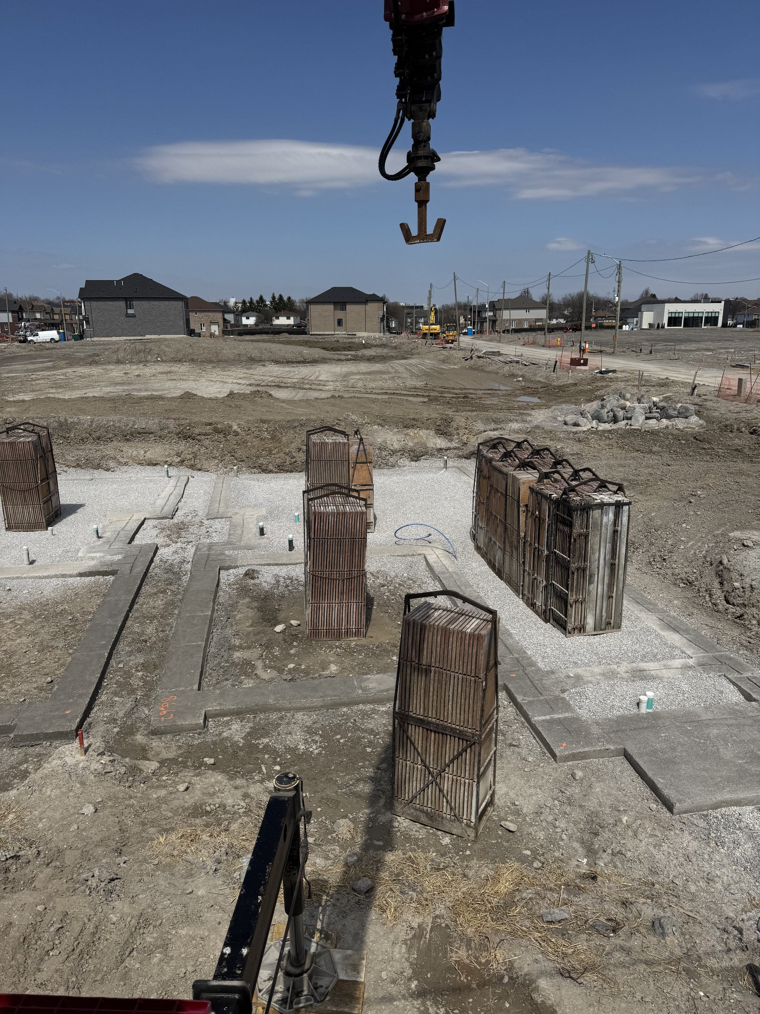 Construction site with foundation and rebar, construction equipment in the background, and a clear blue sky.
