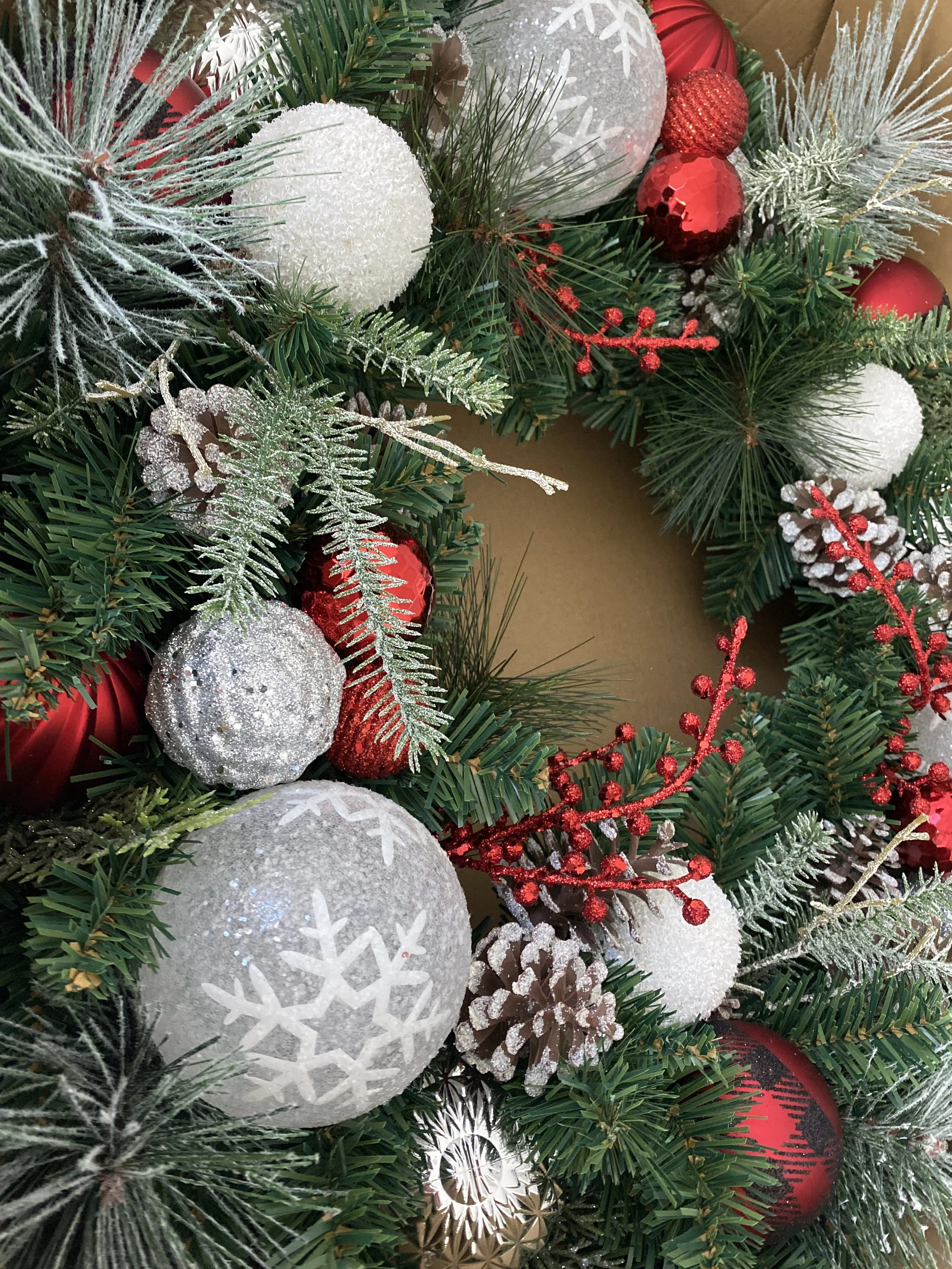 A Christmas wreath decorated with white, red, and silver ornaments, pinecones, artificial snow, and red berries.