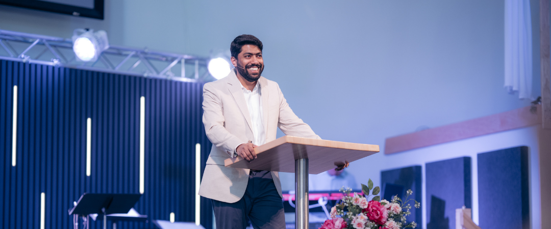 Man smiling and speaking at a podium during an event or conference.