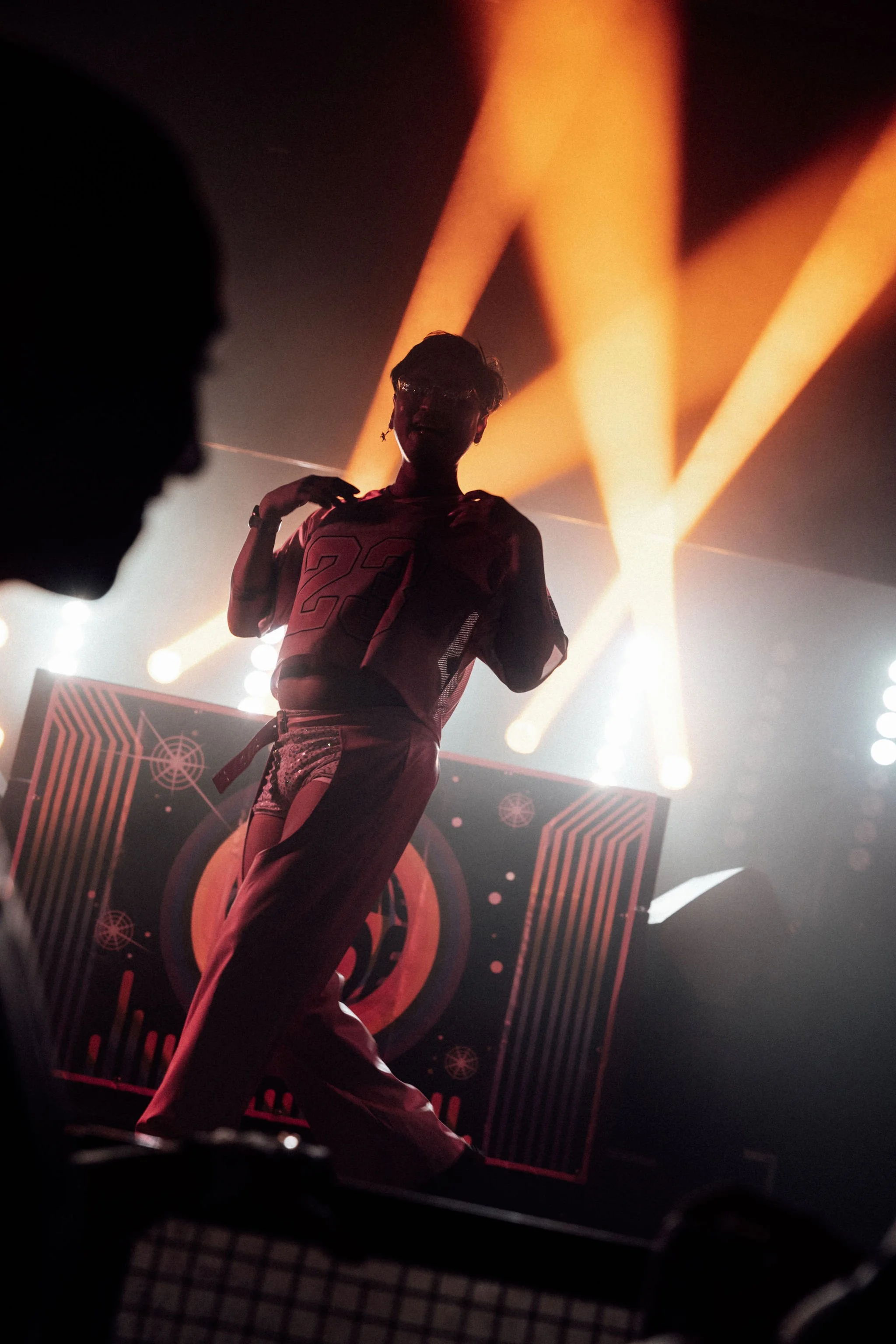 A person wearing a sports jersey with the number 22 stands in front of a stage with bright orange and yellow stage lighting and futuristic graphics.
