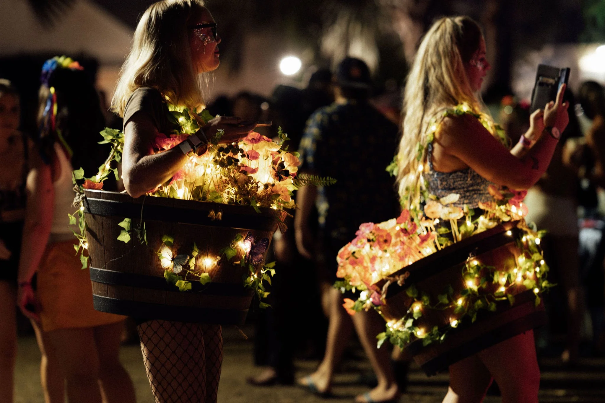 People during a night event carrying decorated lanterns with lights and flowers.