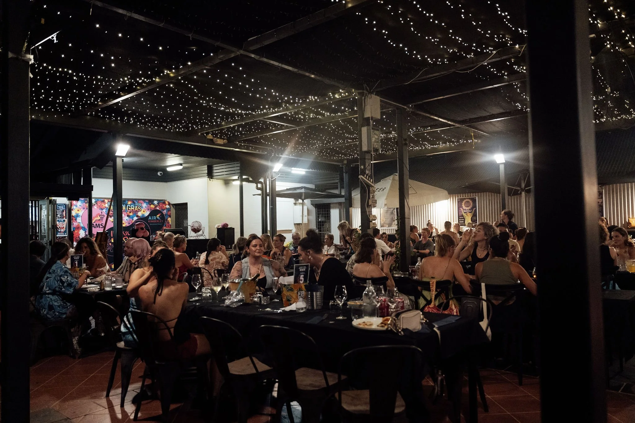 People dining at tables indoors under a dark ceiling decorated with numerous small string lights at night.