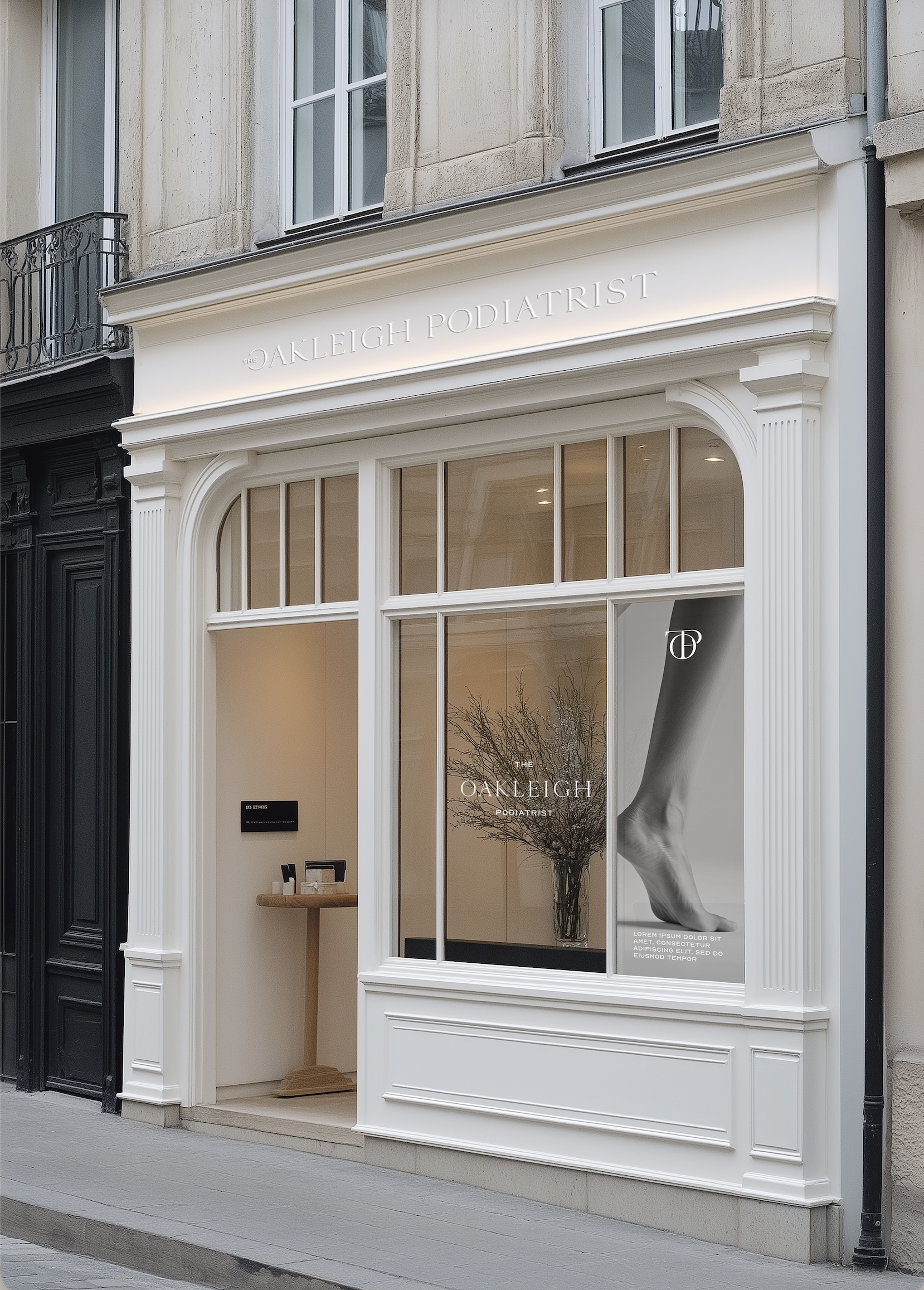 Storefront with white ornate trim, large window displaying a flyer with a black and white photograph of a foot, and the words 'The Oakleigh Podiatrist' on the signage above.