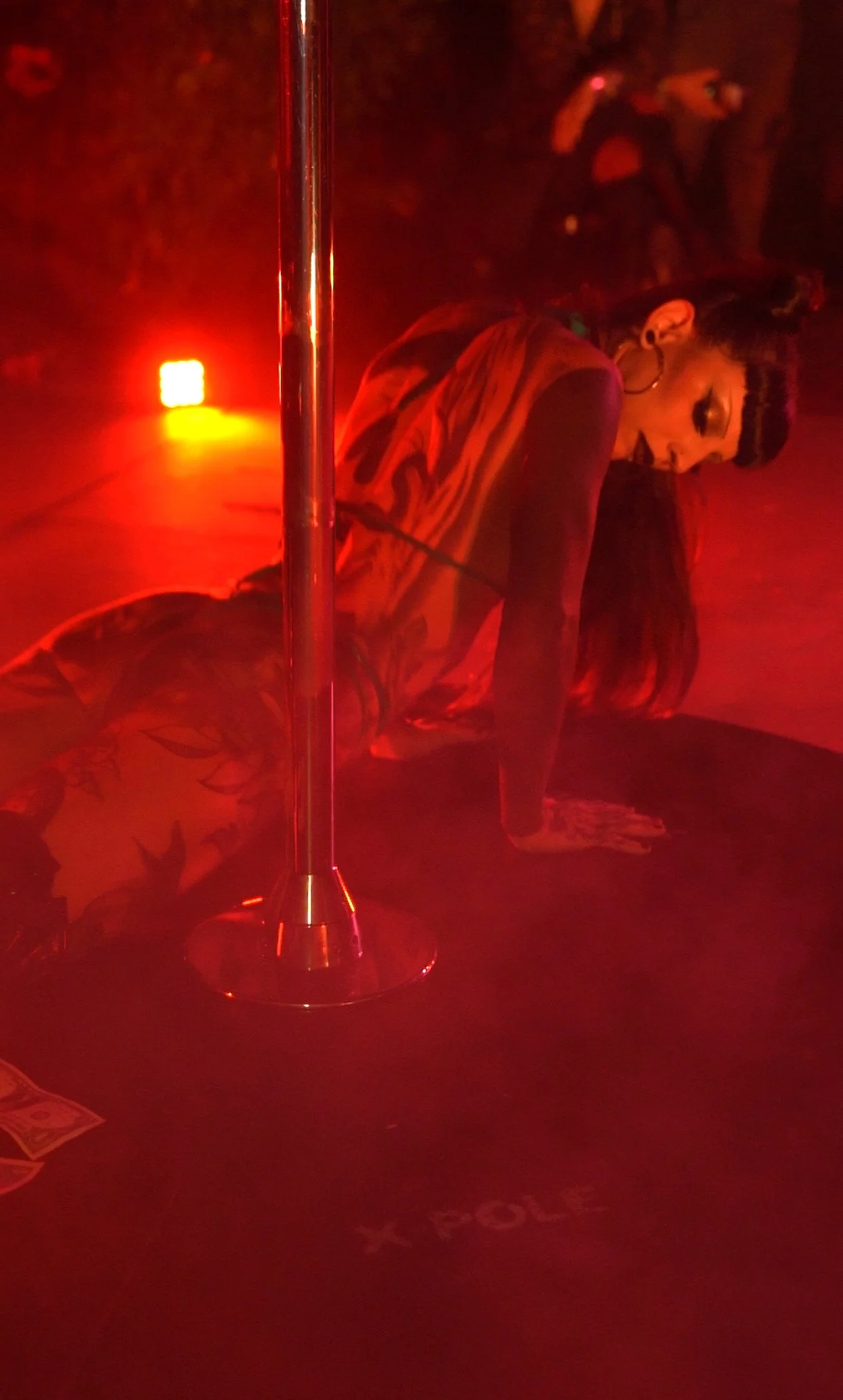 A woman performing a yoga pose in a dark room illuminated by red lighting, with a standing pole in the foreground.