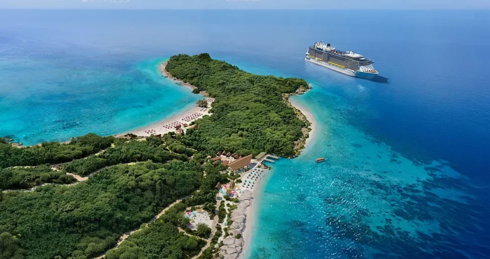 Aerial view of a lush green island with a sandy beach, turquoise waters, and a cruise ship nearby in the ocean.