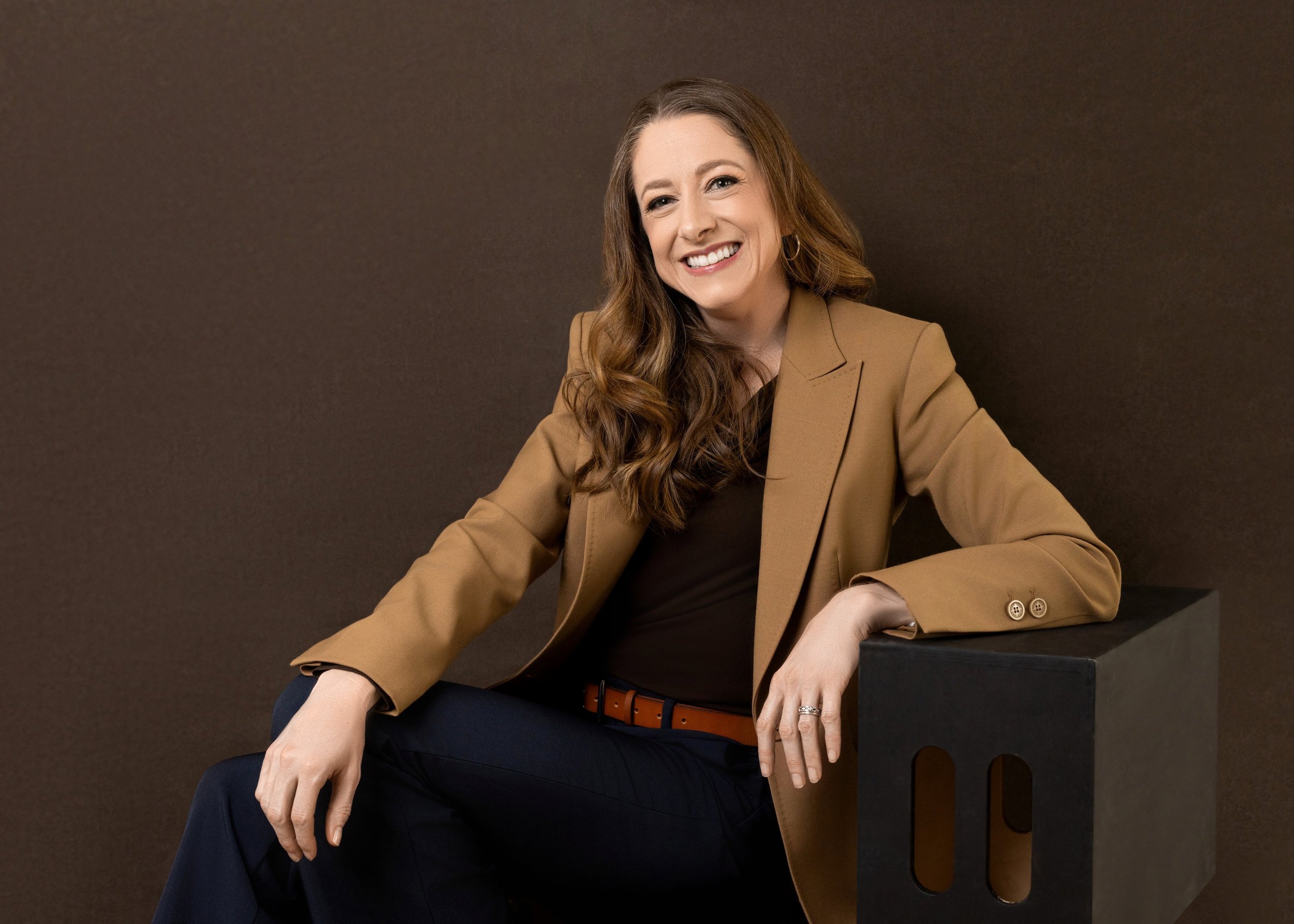 Seated professional portrait with a warm brown background.