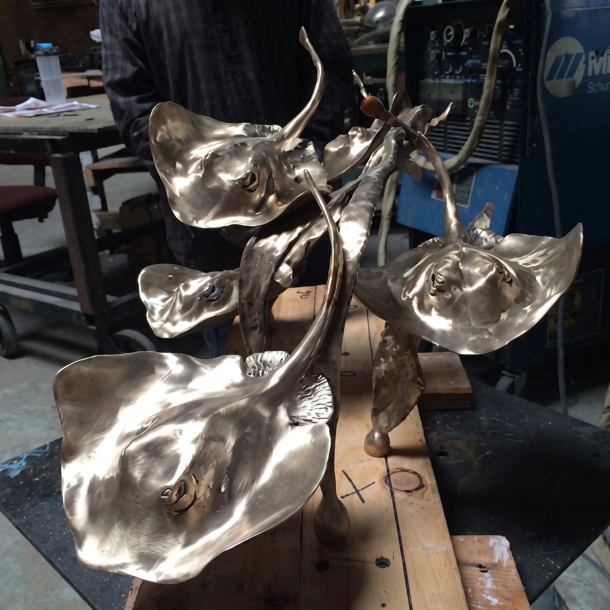 A person holding a metallic sculpture of a horse, seen in a workshop or studio with tools and equipment in the background.