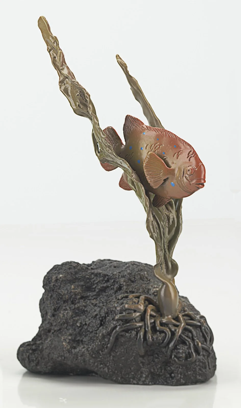 A sculpture of a Garibaldi fish with a plant-like body growing out of a rock, with a plain white background. By Judy Salinsky.