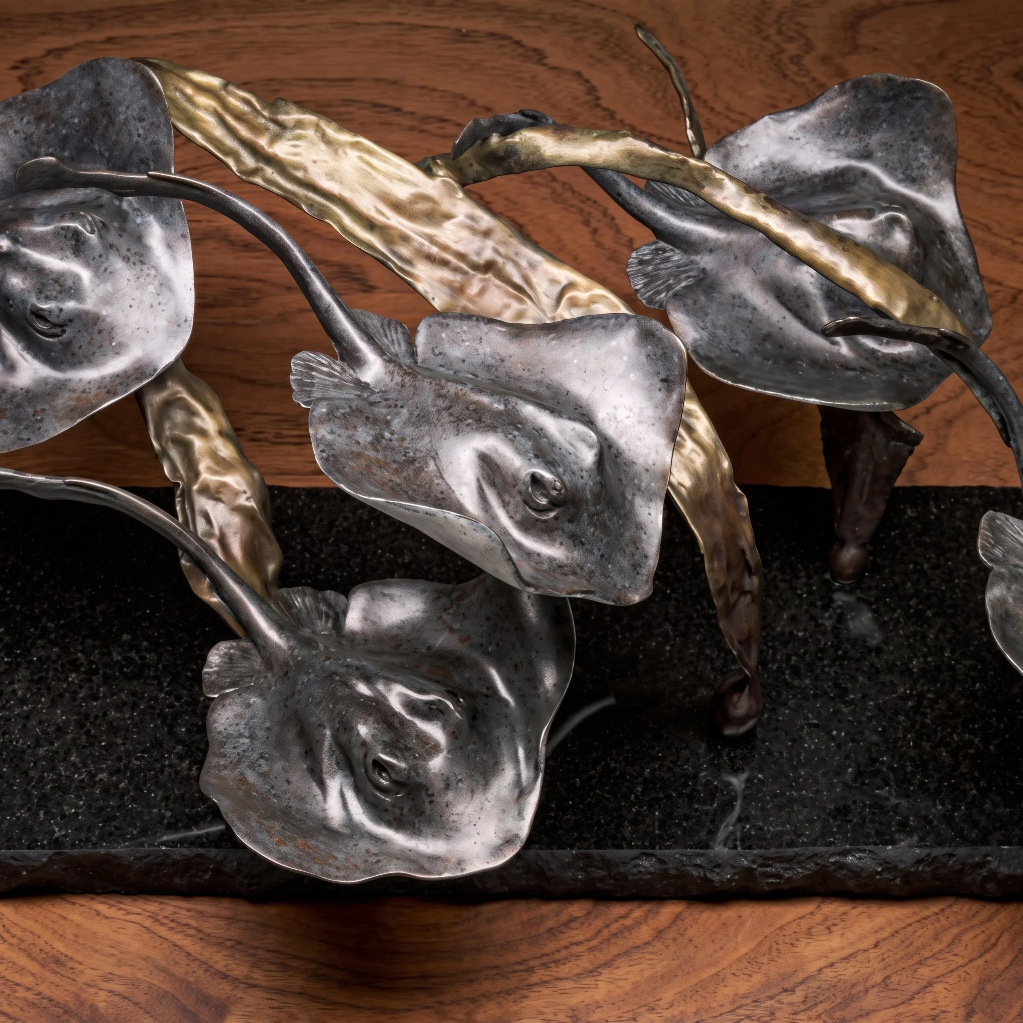 Close-up of a decorative metal sculpture of fish and abstract elements, placed on a wooden surface.