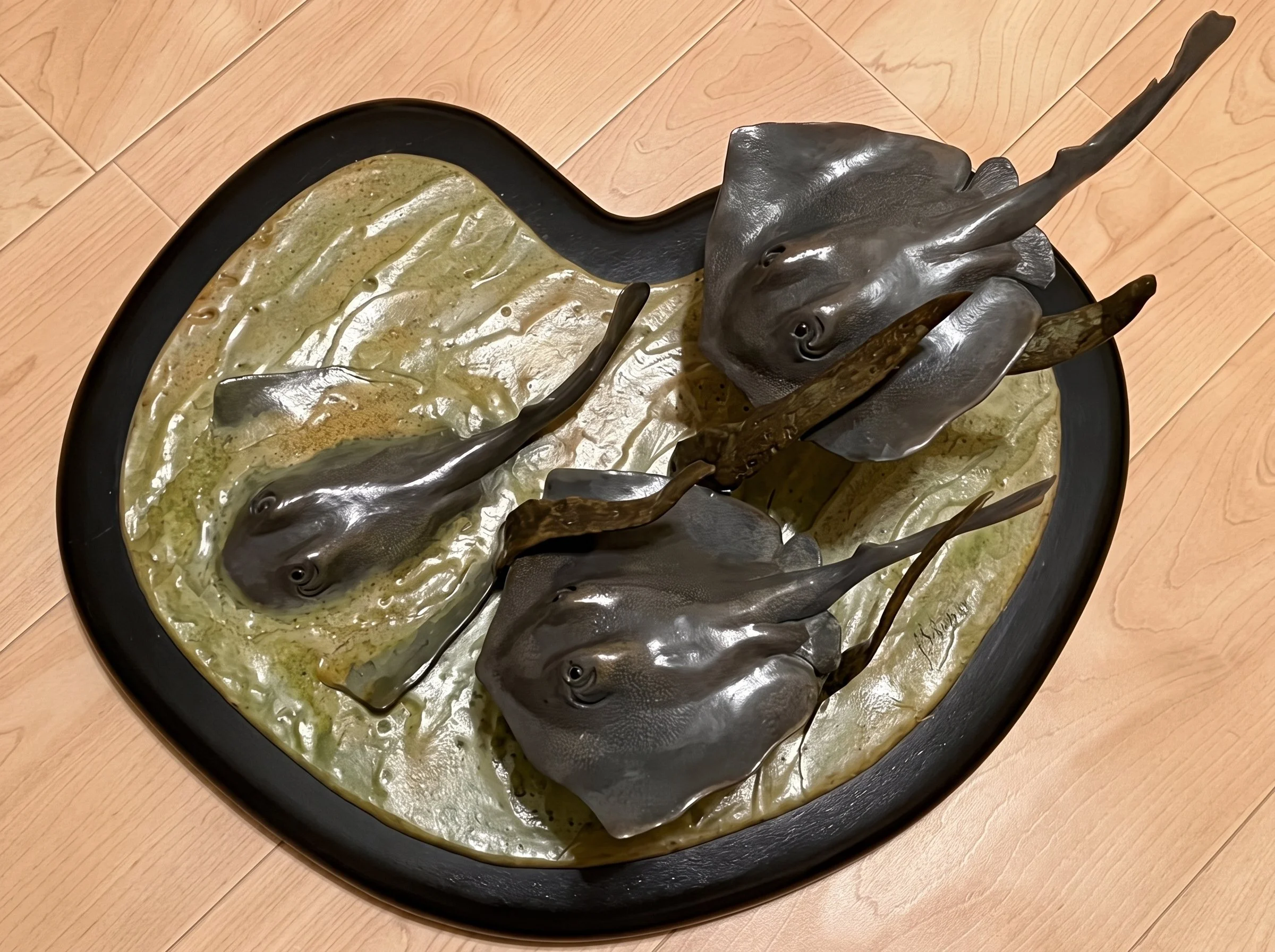 A bronze sculpture of three stingrays lying on sand representing ocean movements. By Judy Salinsky