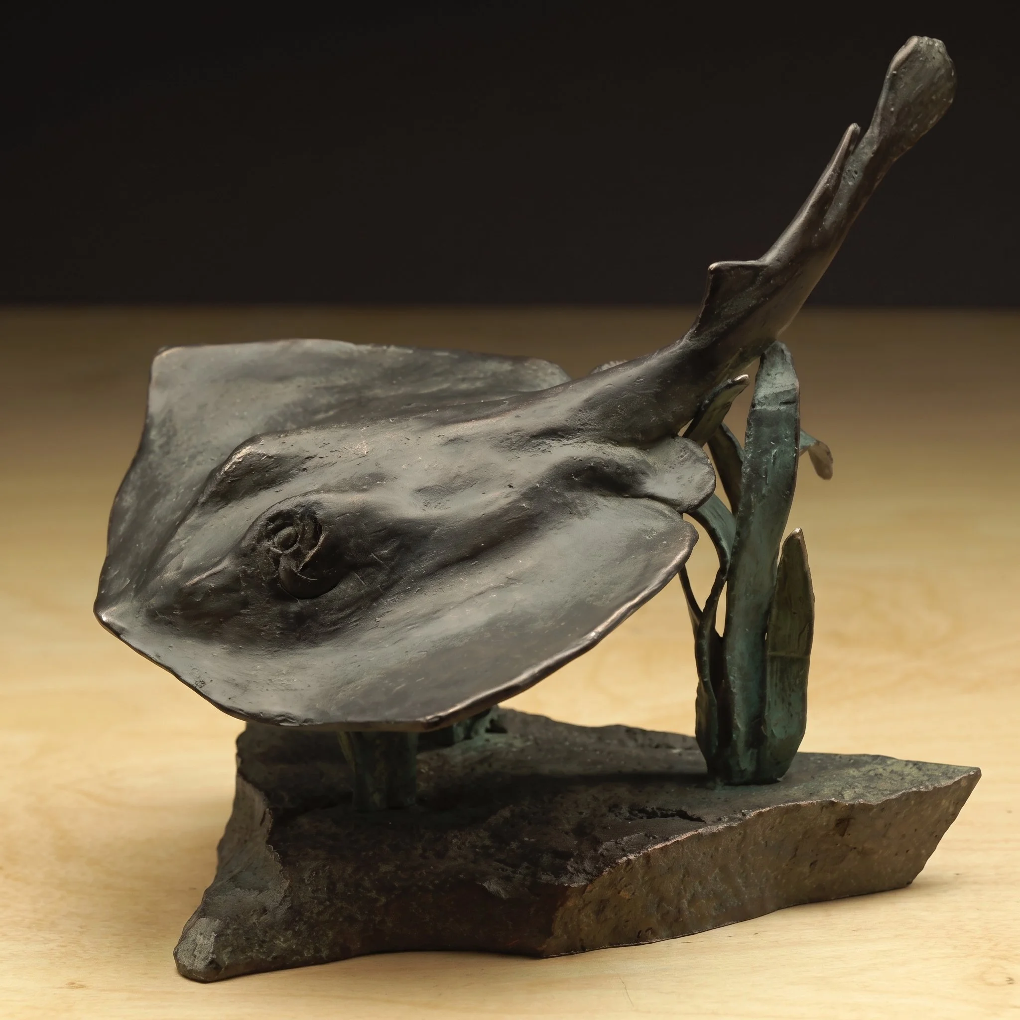 Close-up of a metallic sculpture resembling a dog's head with an elongated snout, pointed ears, and detailed features, mounted on a rough stone base.