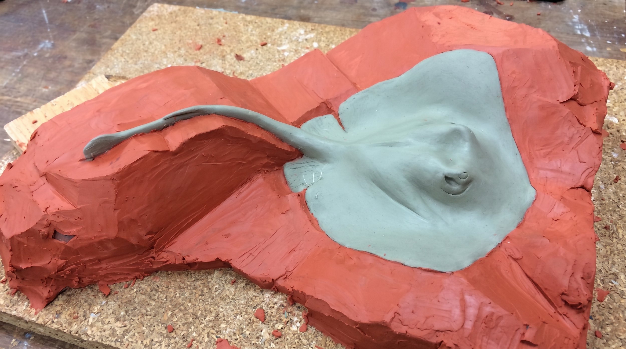 A clay sculpture of a stingray lying down, on red-colored clay. By Judy Salinsky