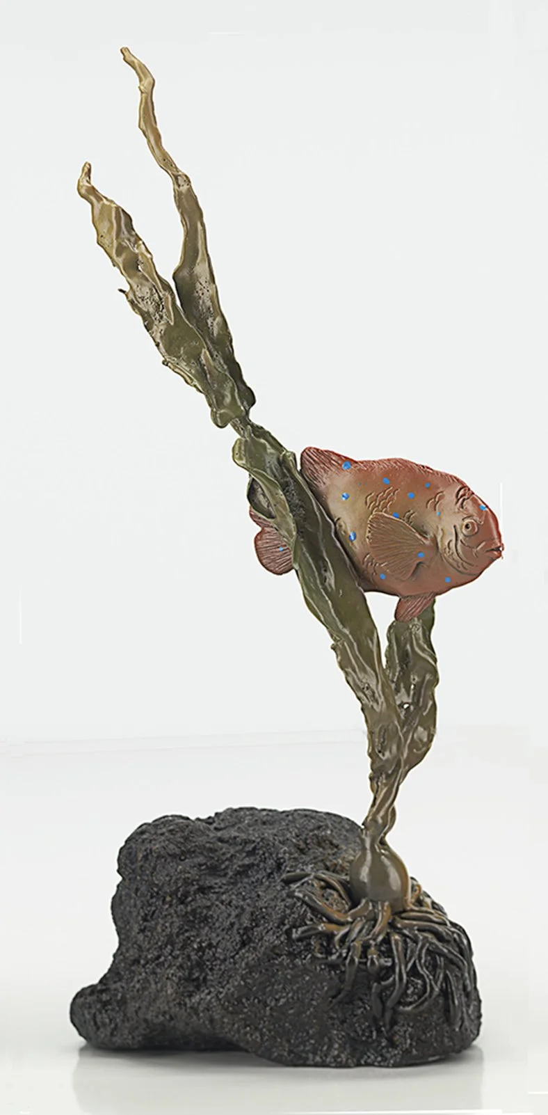 A sculpture of a fish attached to a plant growing out of a rock, with roots visible at the base. By Judy Salinsky.