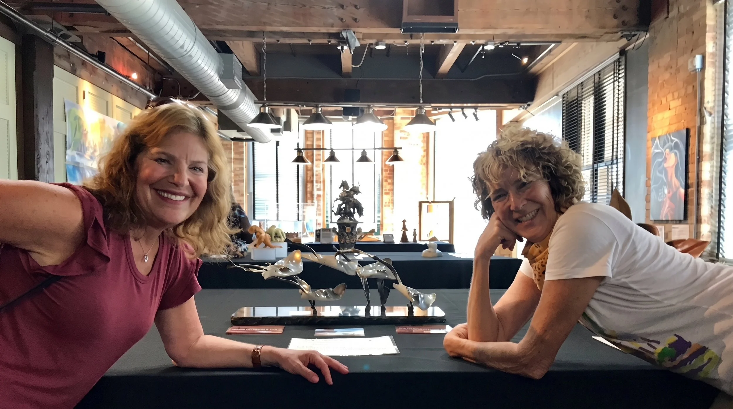 Judy and friend smiling after Judy Salinsky beat cancer with the award wining sculpture " The Fever" on the table.