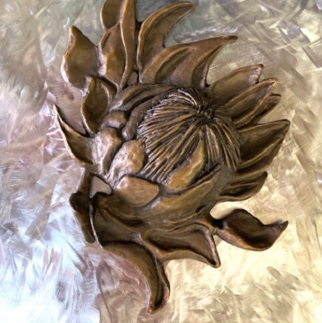 Metallic rose sculpture with detailed petals and leaves, placed on crinkled paper.