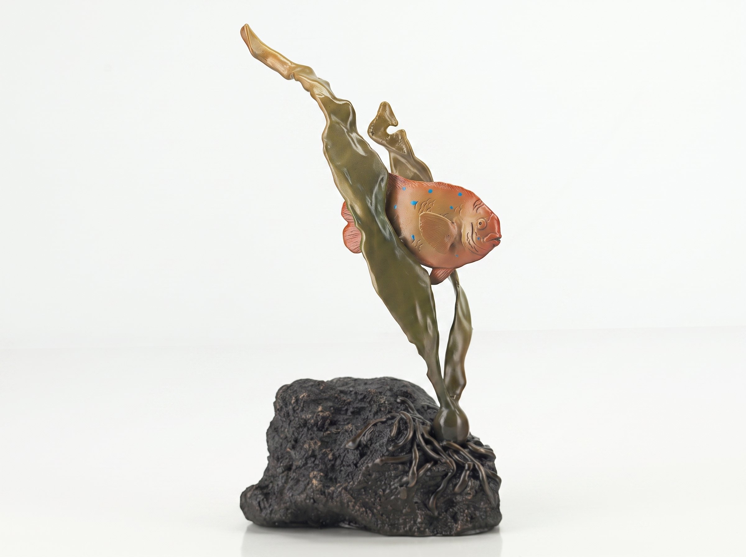 A sculpture of a Garibaldi fish jumping out of dark volcanic rock, with greenish liquid flowing upward, against a plain white background. By Judy Salinsky.