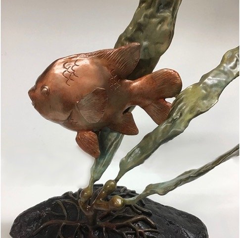 A sculpture of a Garibaldi jumping out of water with stylized waves and a black rock base.