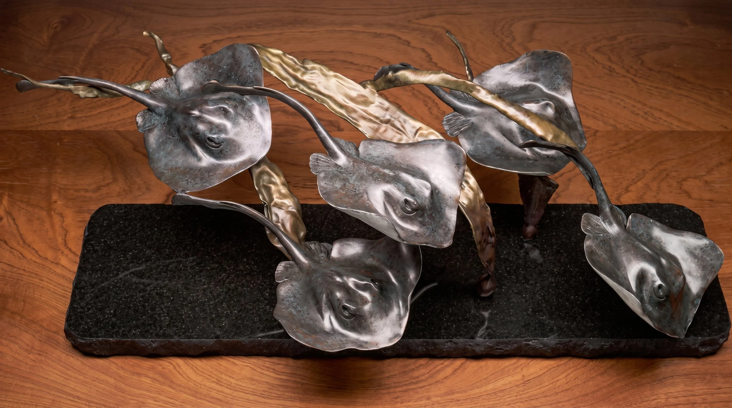 A metal sculpture of multiple dolphins on a black base, set on a wooden surface.