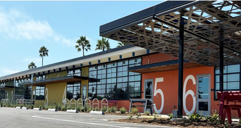 Colorful building with numbered sections 3 to 6, large glass windows, outdoor seating, and palm trees in the background.
