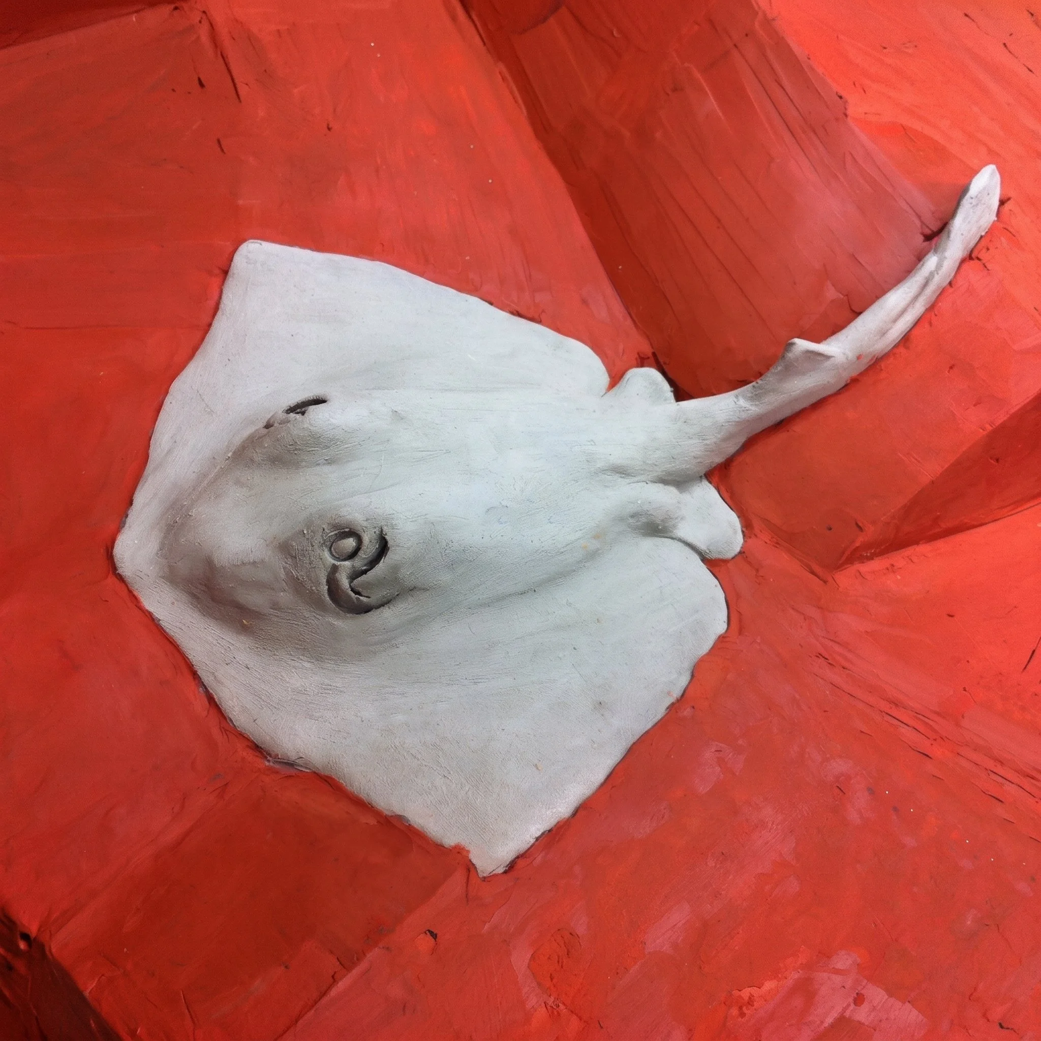 A painted model of a whale with white and gray coloring, lying on an orange wooden surface.