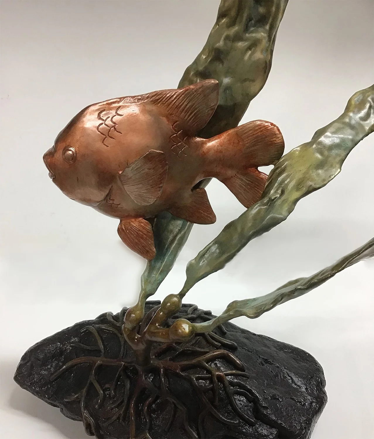 Garibaldi Mama, a bronze made fish sculpture with flowing metallic fins, mounted on a dark, textured base with roots or tendrils.