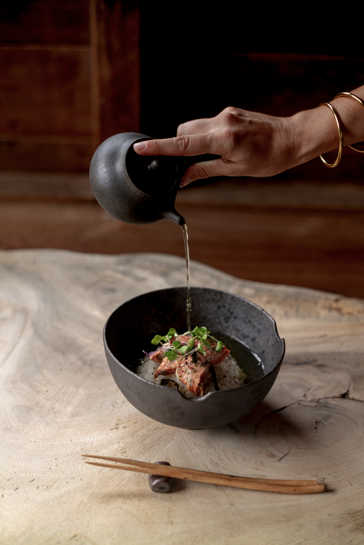 Pouring warm broth from a clay pot into a dark bowl