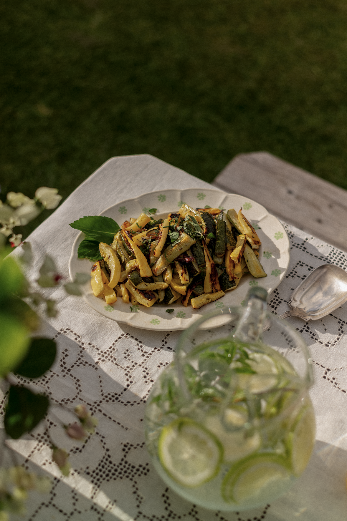 A plate of herbed pasta and cucumber drinks on a lace cloth outdoors