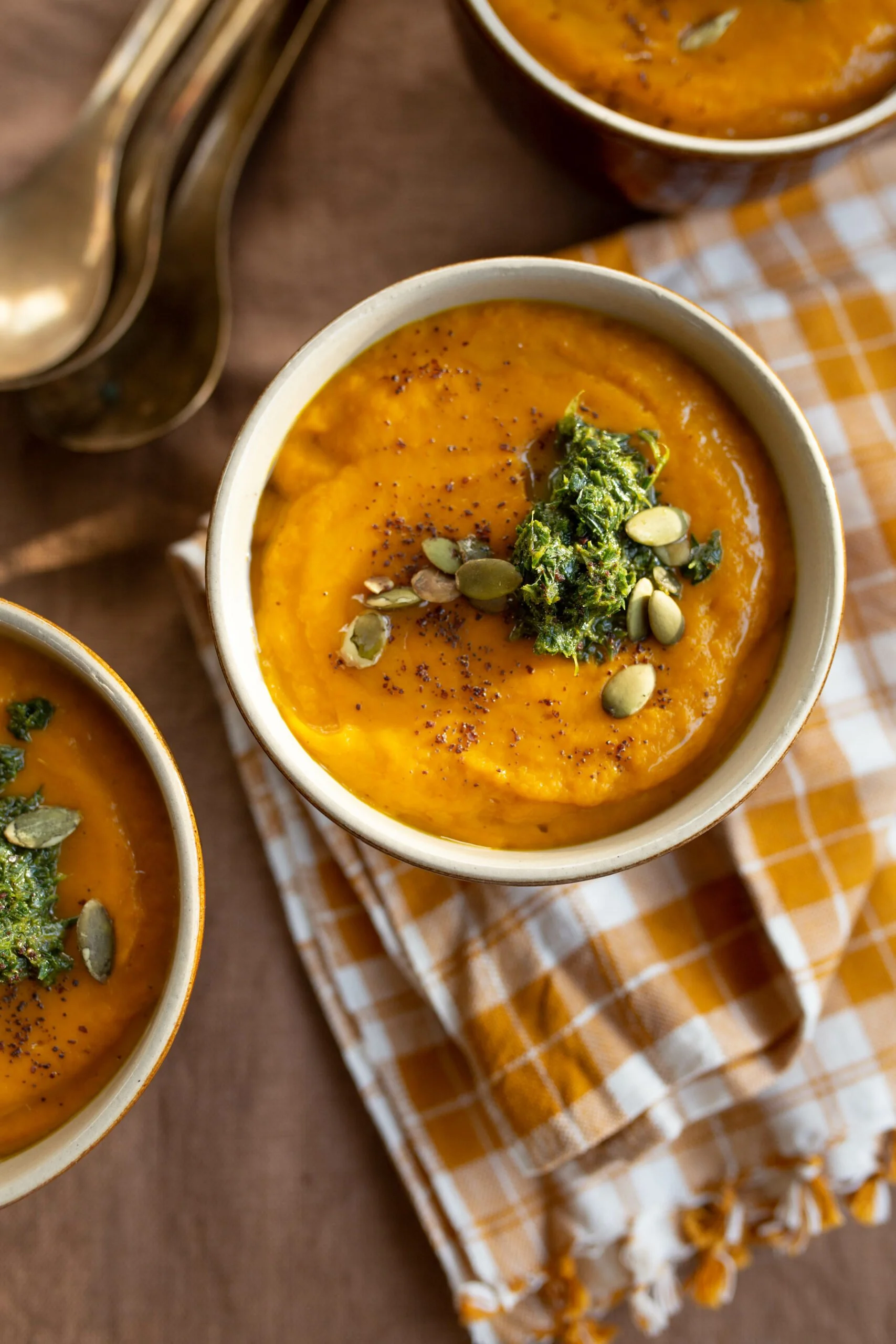 Two bowls of squash soup topped with herb pesto and seeds