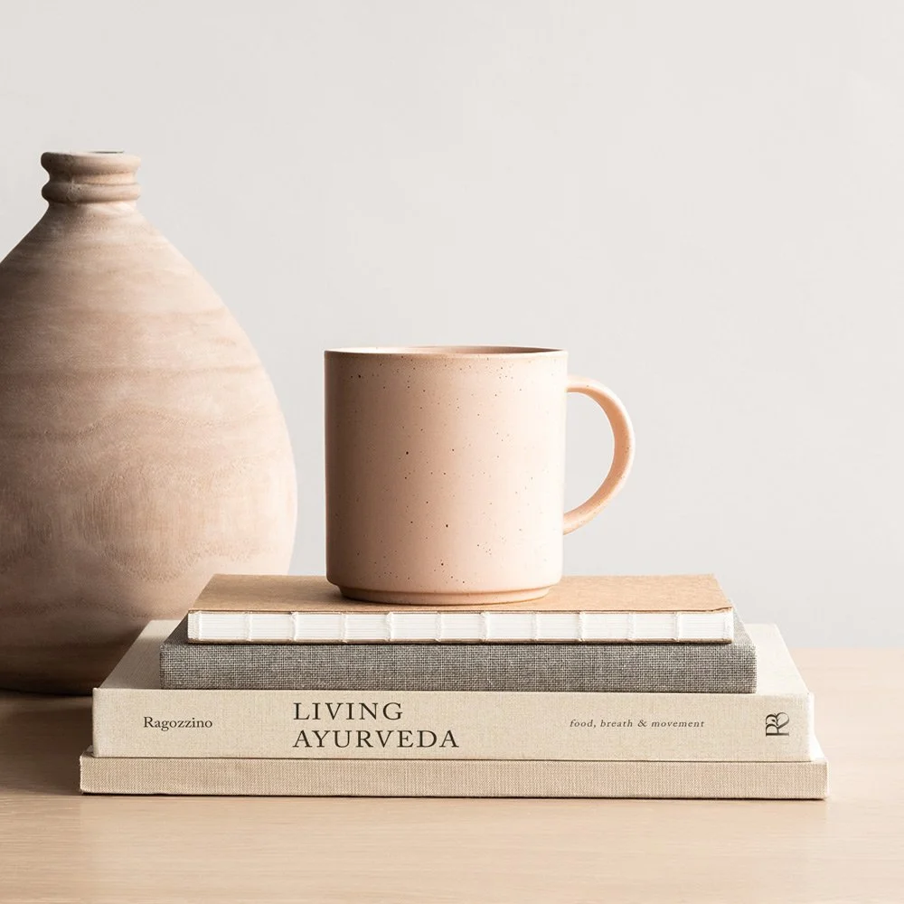The Living Ayurveda book stacked with a mug and a clay vase