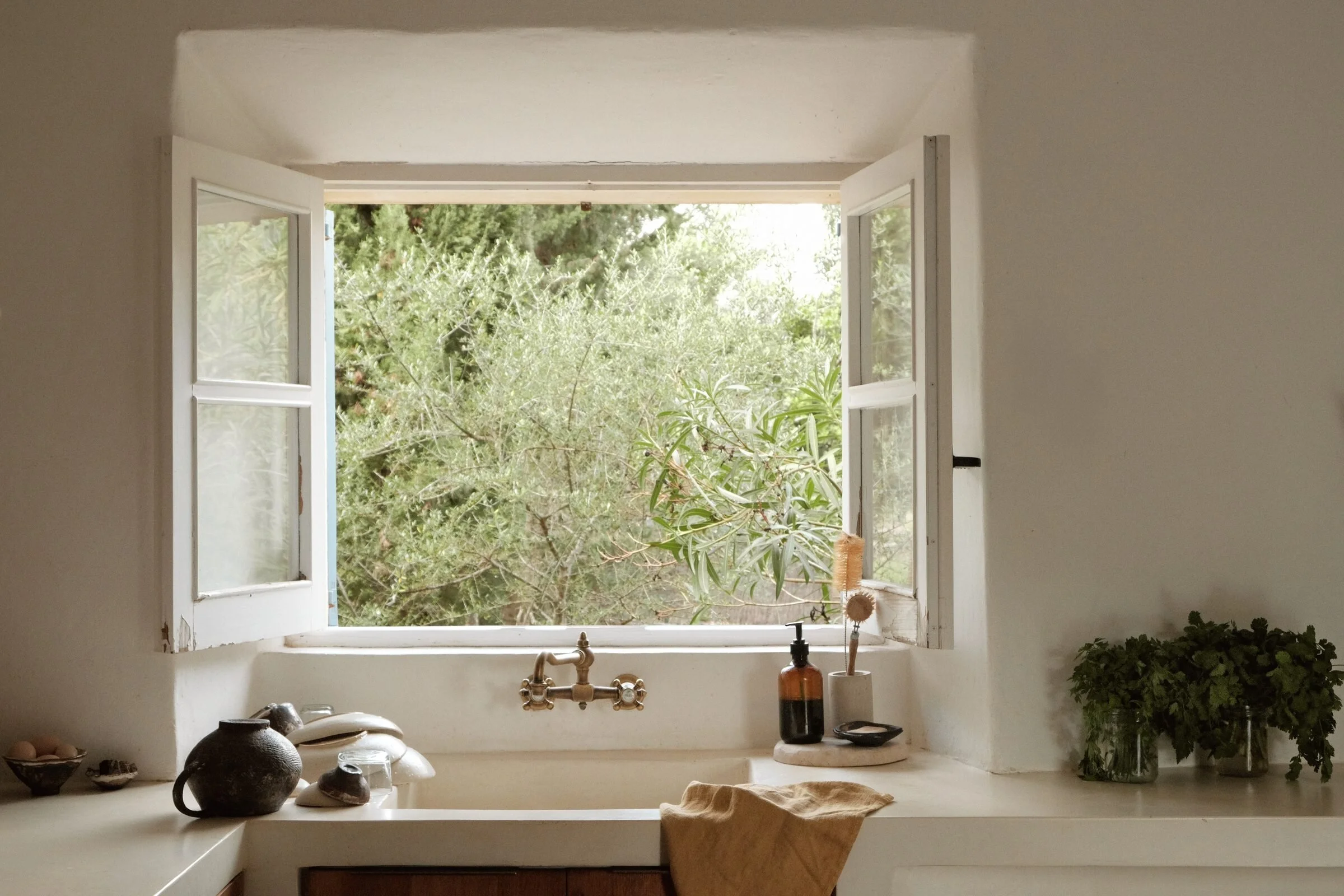 An open kitchen window above a plaster sink, looking out onto olive branches