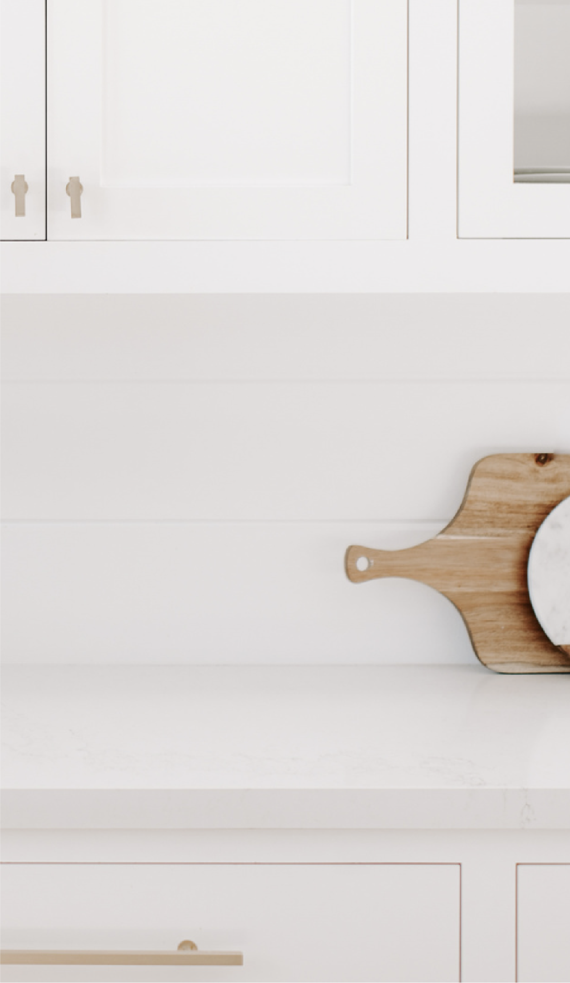 White kitchen cabinets with silver handles, a wooden cutting board with a knob, and a bowl on top.