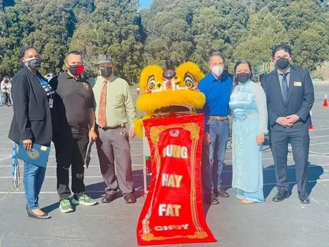 Christy with other city officials all wearing face masks, behind a sign that says Kung Hay Fat Choy, which means Happy New Year in Cantonese