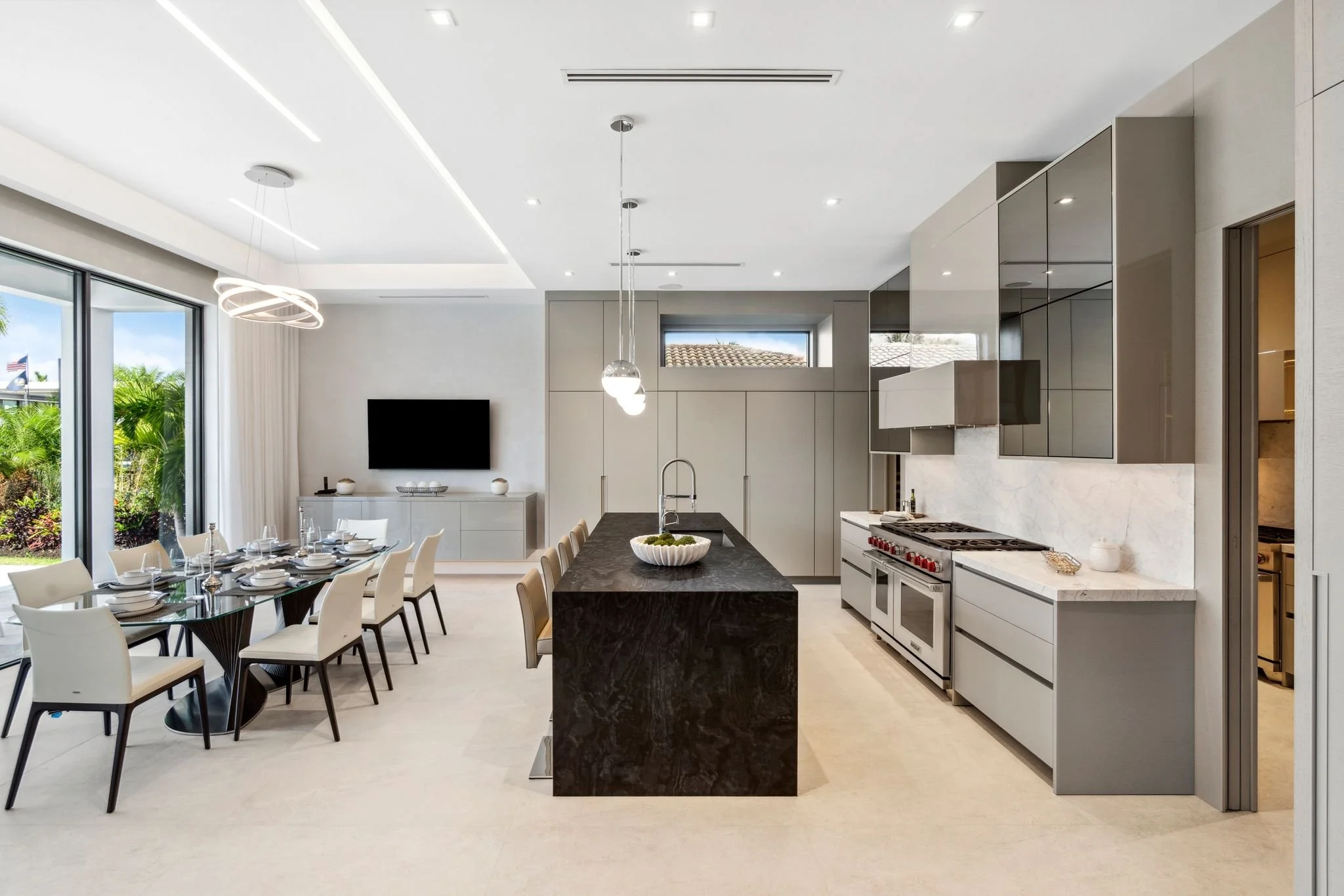 Modern kitchen and dining area with white walls and ceiling, black marble island, stainless steel appliances, built-in cabinets, large sliding glass door, and outdoor greenery.