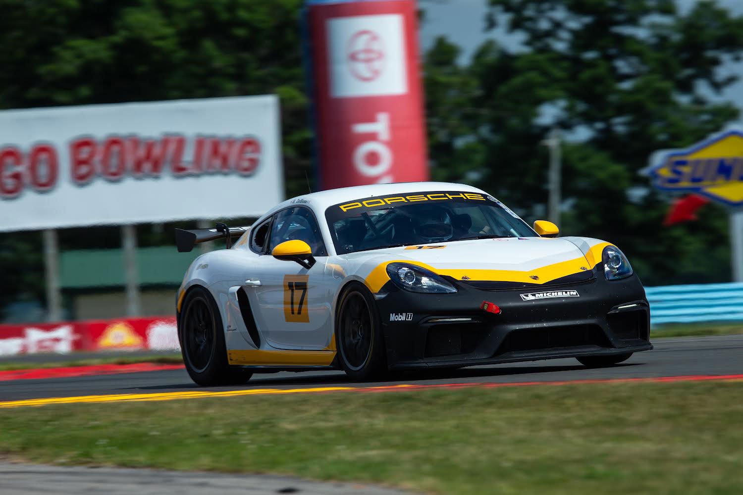 A white and black Porsche race car with yellow accents, numbered 17, speeding on a race track.