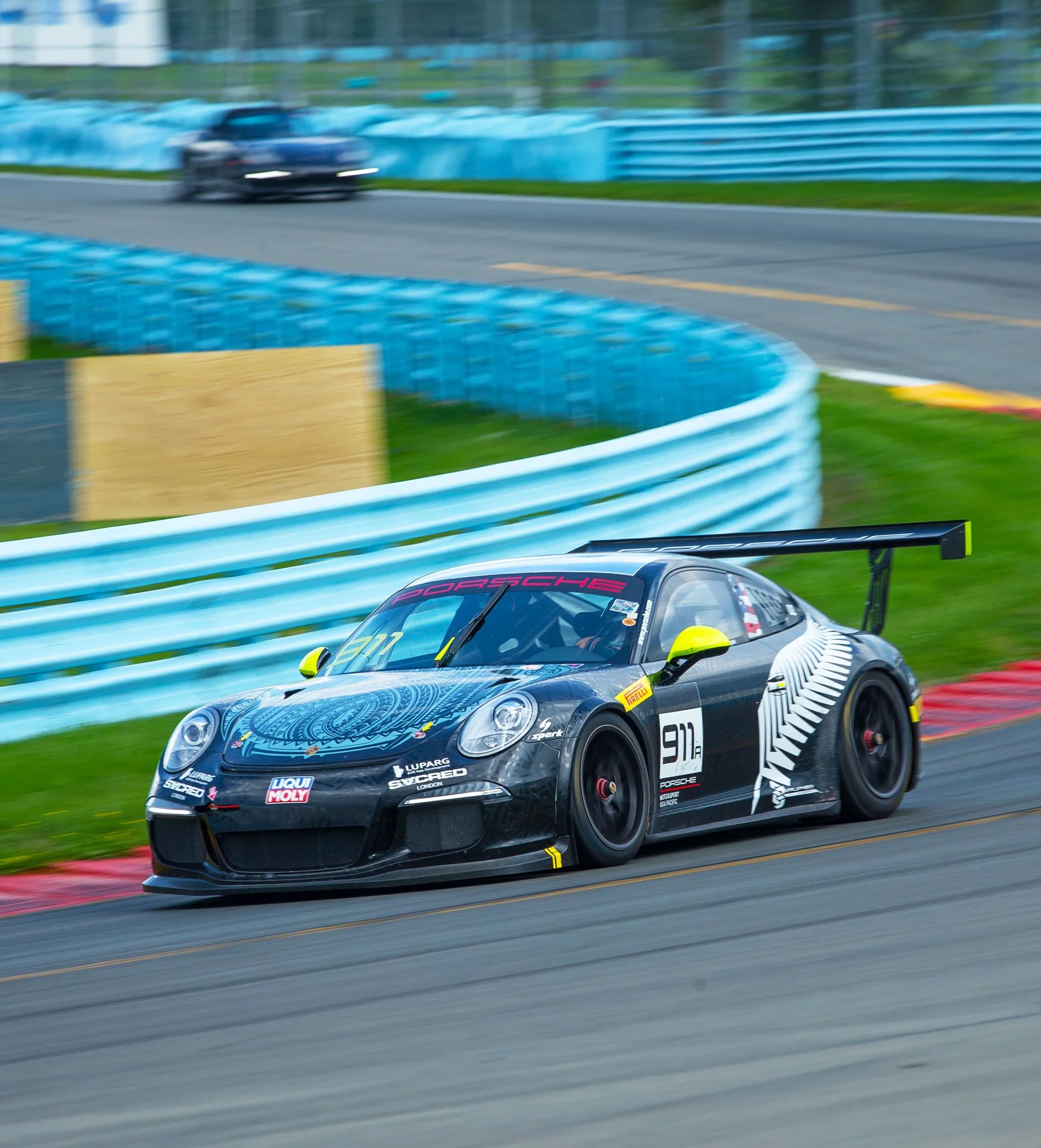 A black Porsche race car speeding on a racetrack with blue barriers and green grass sides.